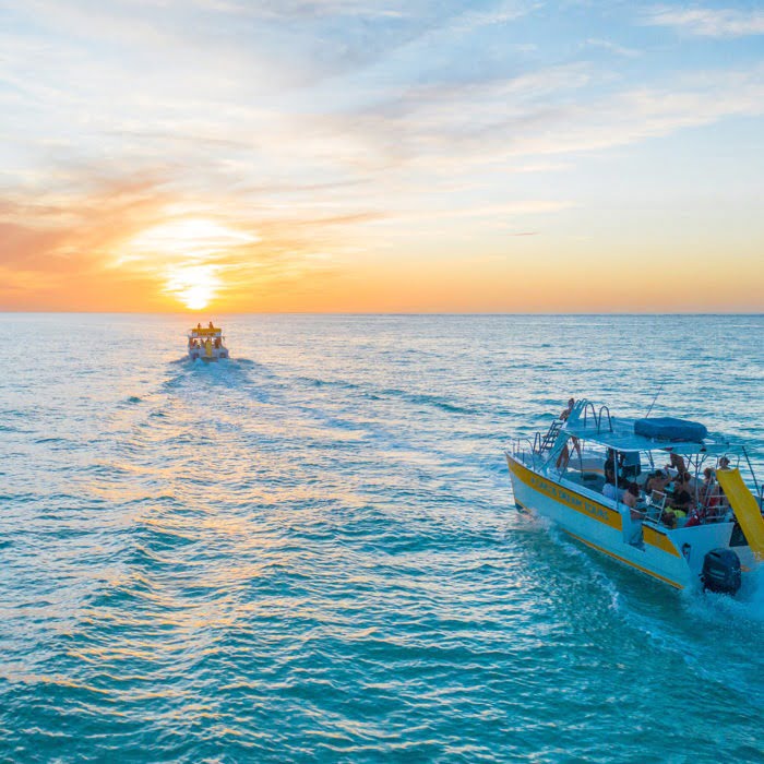 Two boats travel towards the sunset horizon