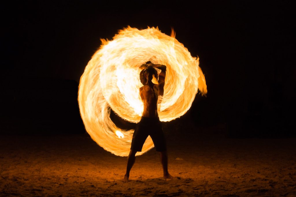 Person spinning a large fire hoop at night on a beach.