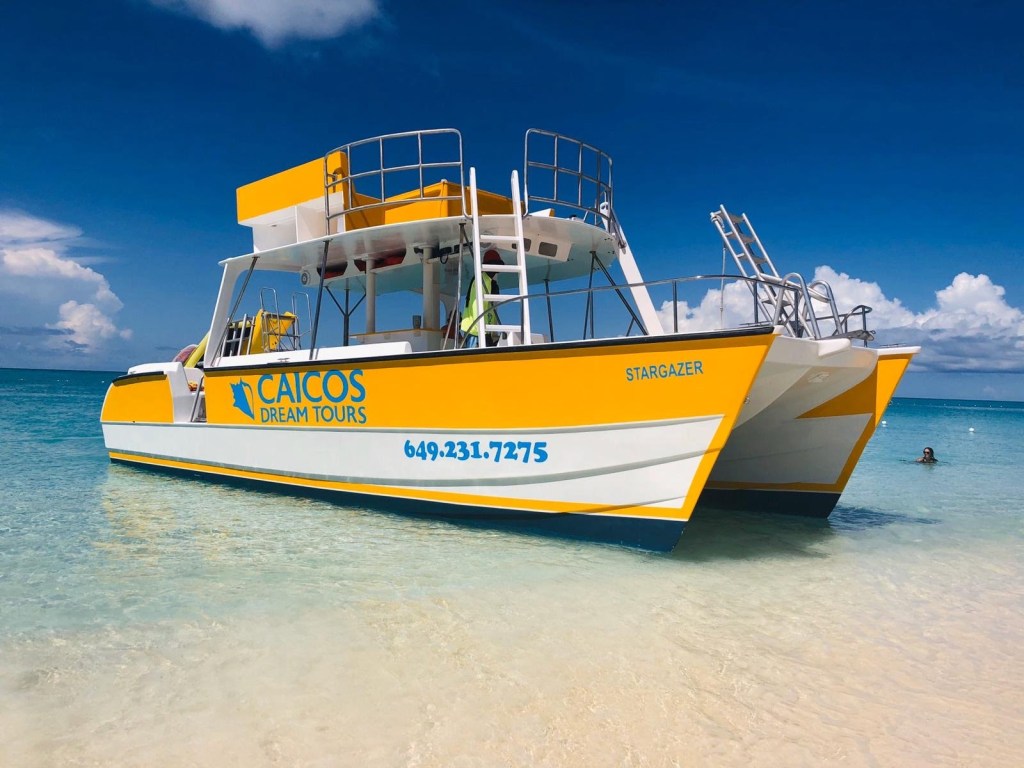 Yellow tour boat on clear water near a sandy beach under a blue sky.