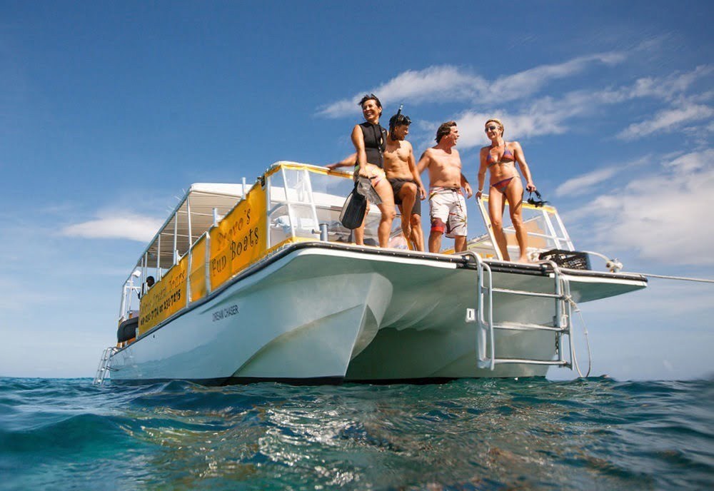 Four people in swimwear stand on a boat, holding snorkel gear.