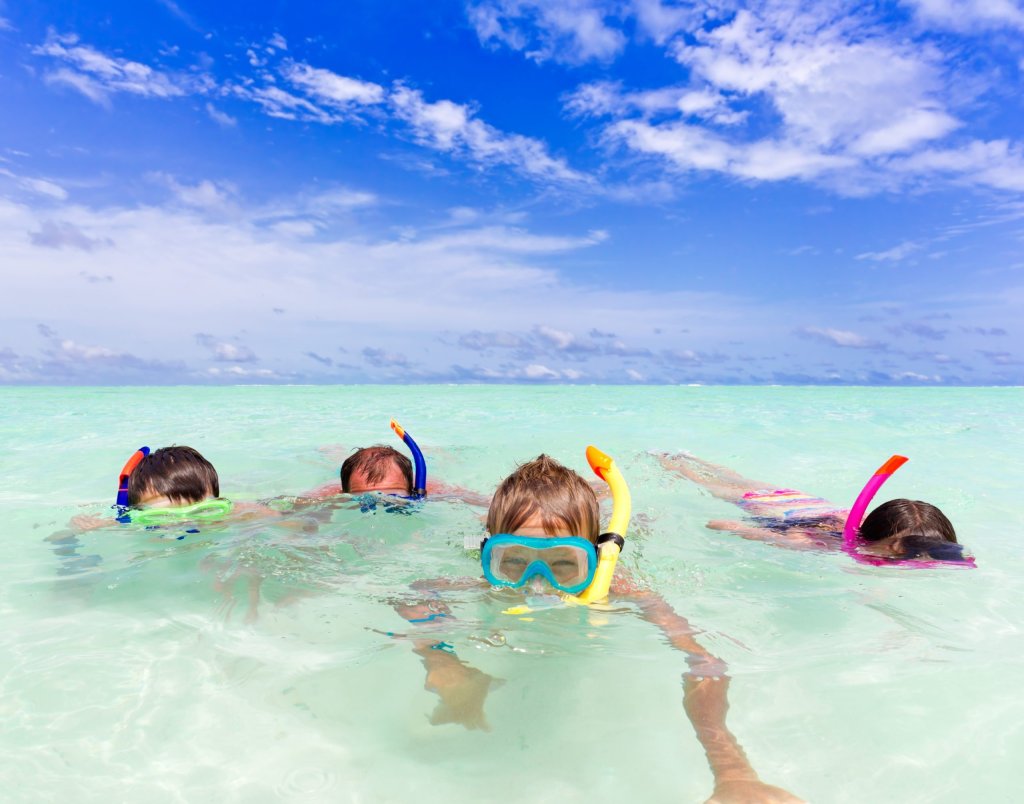 Family snorkeling in clear ocean water under a bright blue sky.
