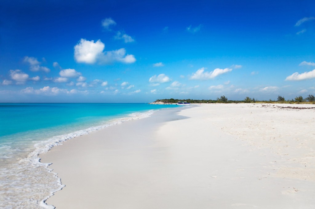 Pristine beach with white sand, turquoise water, and blue sky with few clouds.