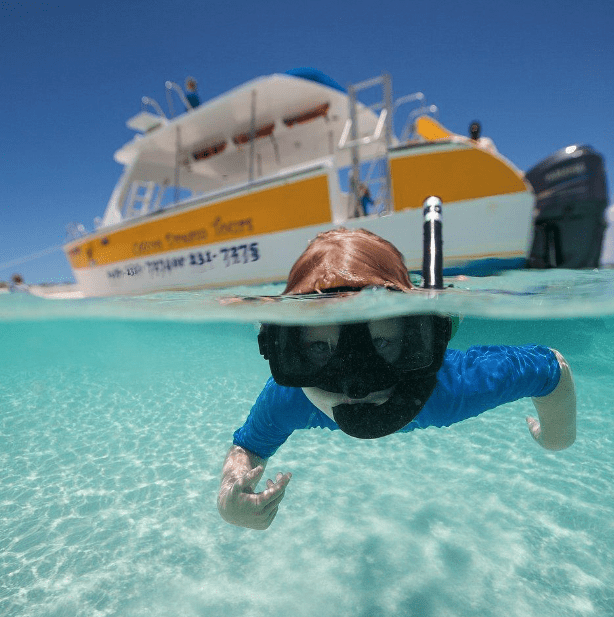 Child snorkeling underwater near a boat in clear turquoise sea.