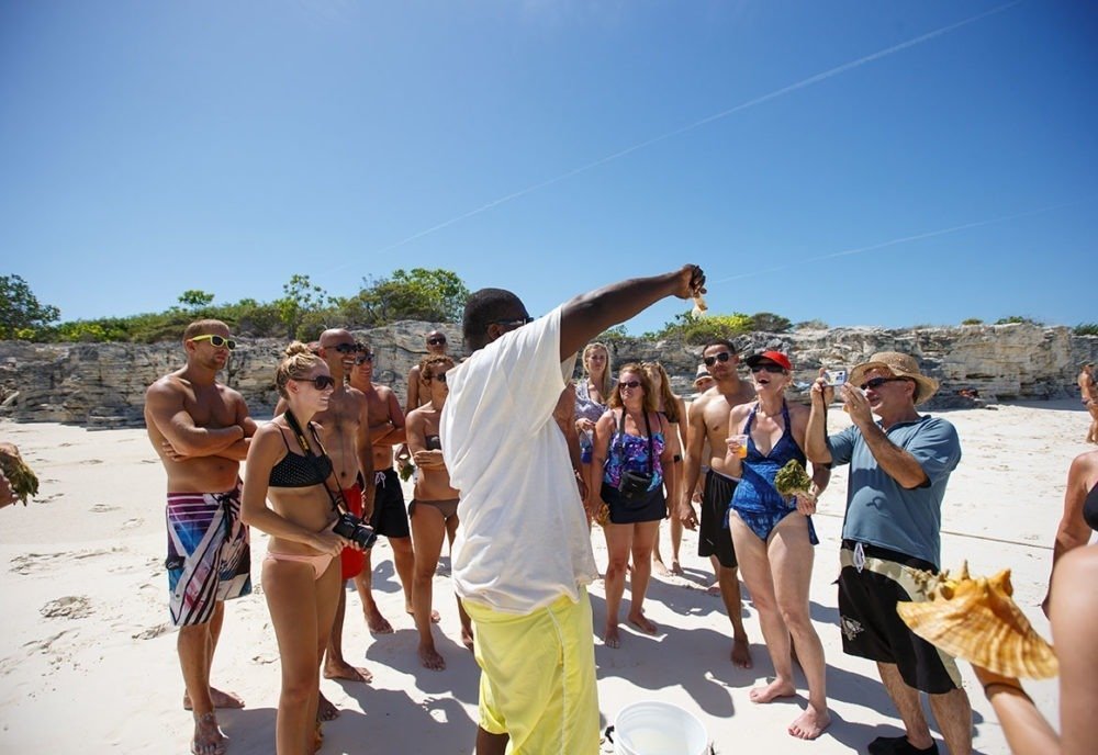 Group of people on a beach listening to a speaker holding a seashell.