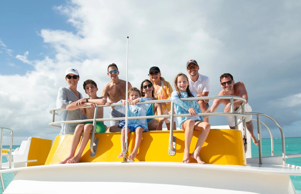 Group of people smiling on a boat with a yellow railing, under cloudy skies.