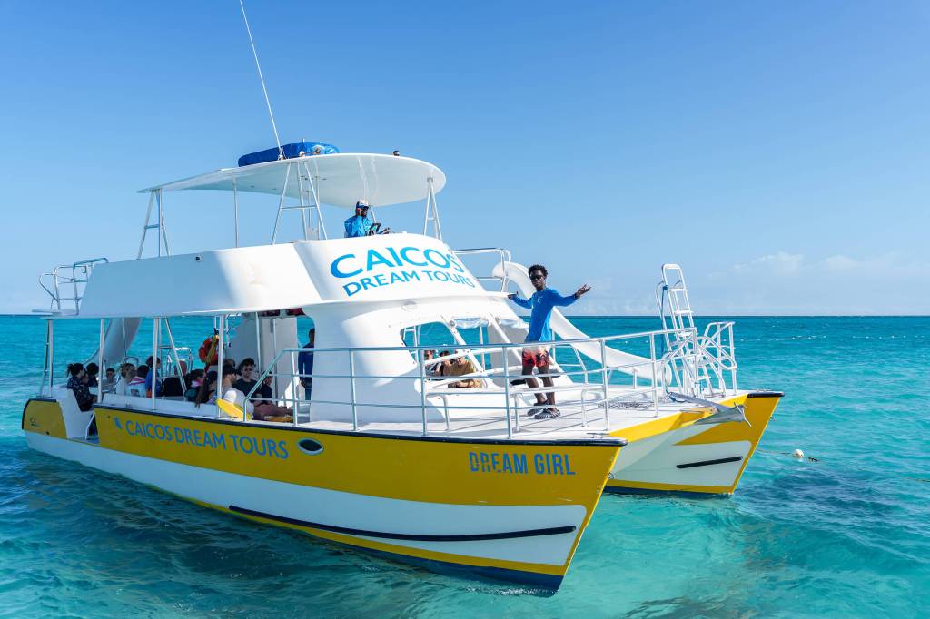 Catamaran with tourists on turquoise water, labeled 'CAICOS DREAM TOURS.'