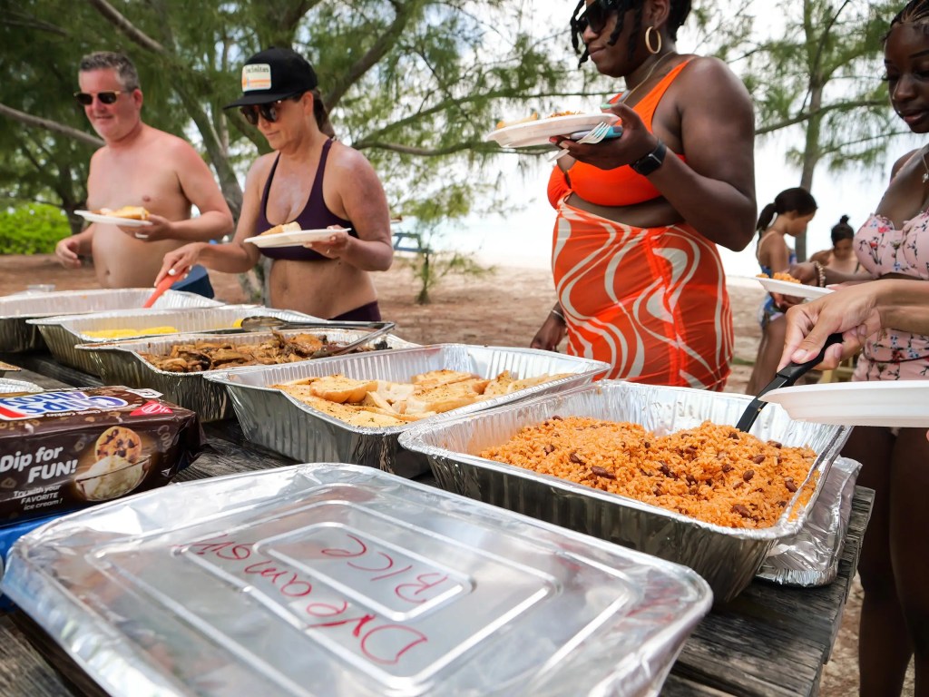 People serving food from trays at an outdoor picnic.