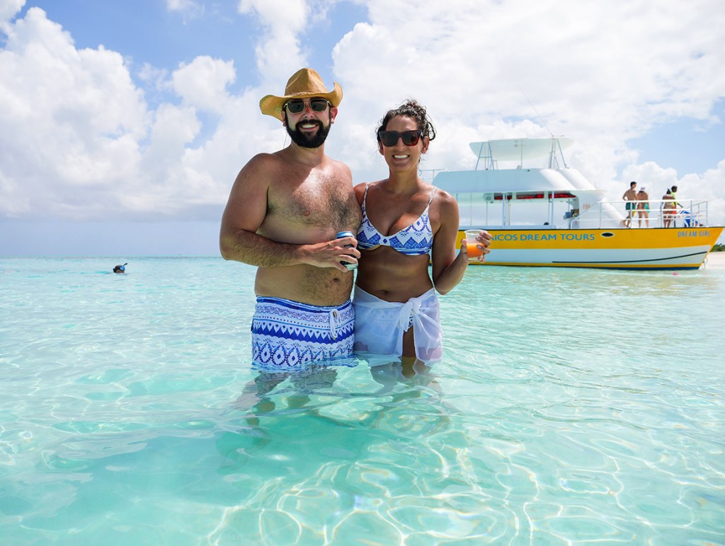 Two people stand in shallow water near a boat under a clear sky.