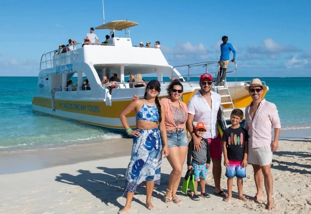 Group of people posing on a beach near a boat.