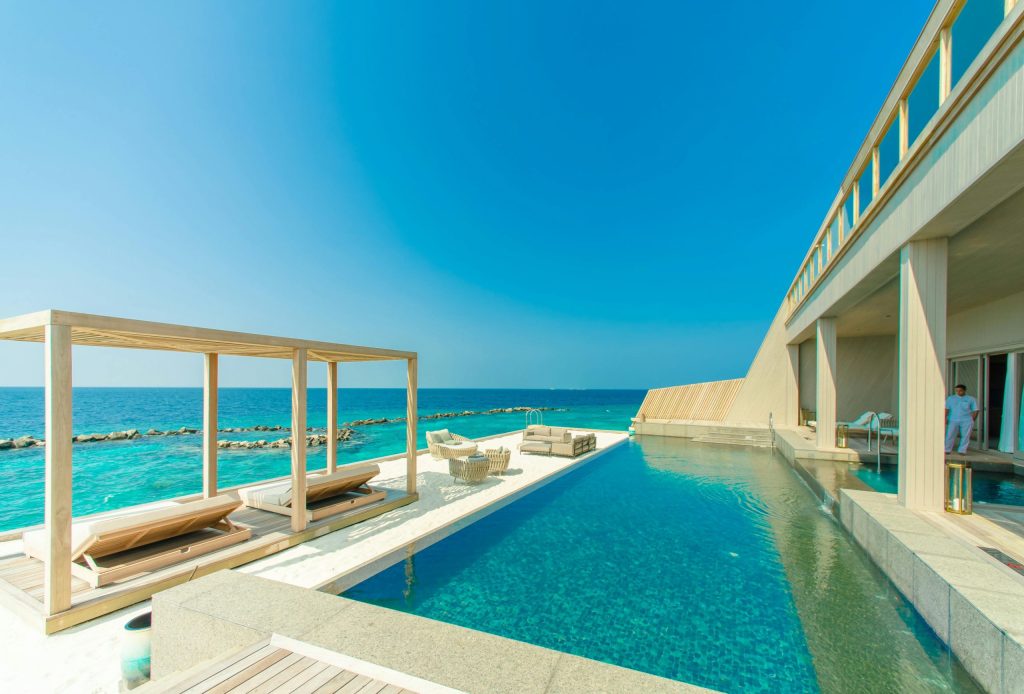 Modern oceanfront villa with pool, sun loungers, and clear blue skies.