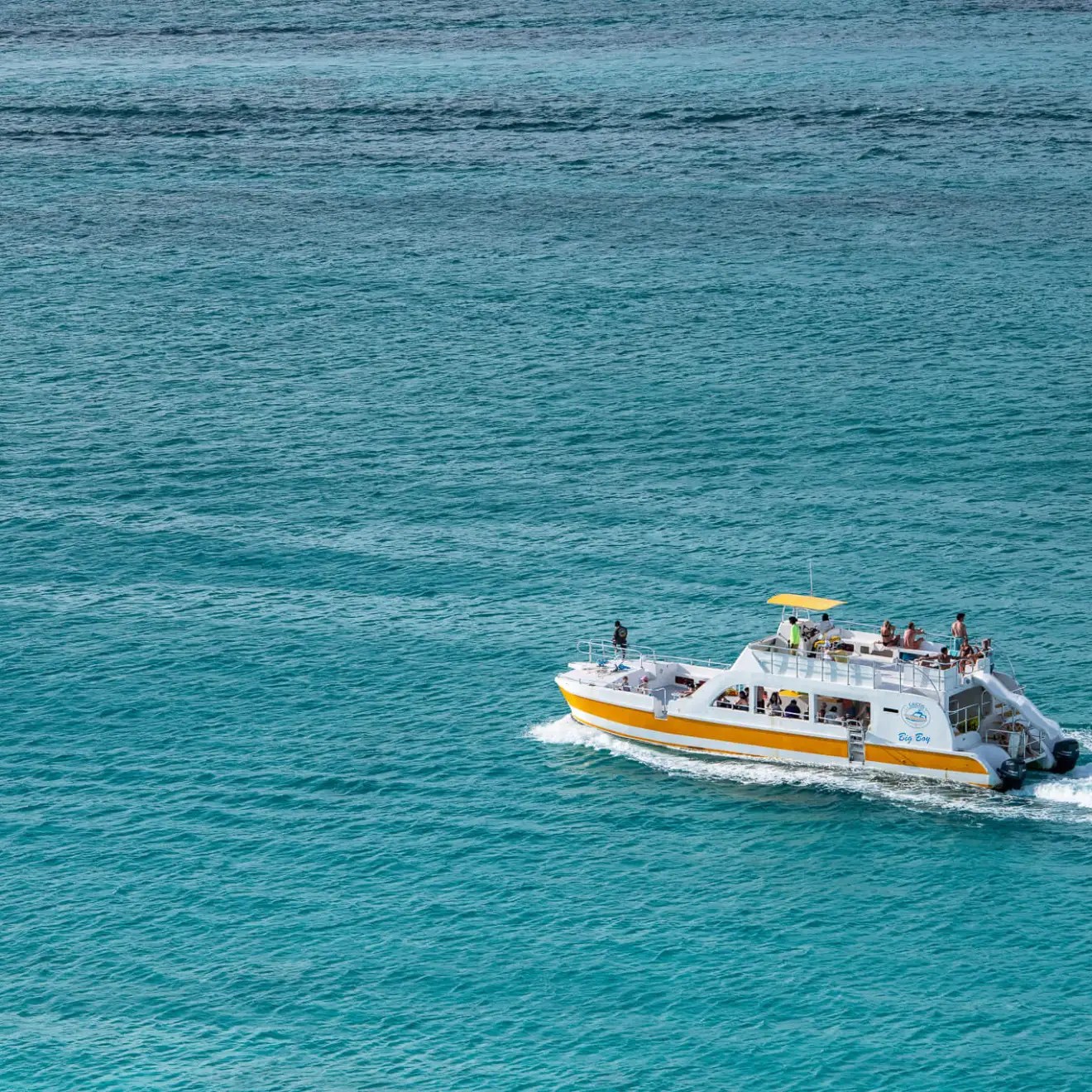 White and yellow ferry boat on blue ocean with people on board.