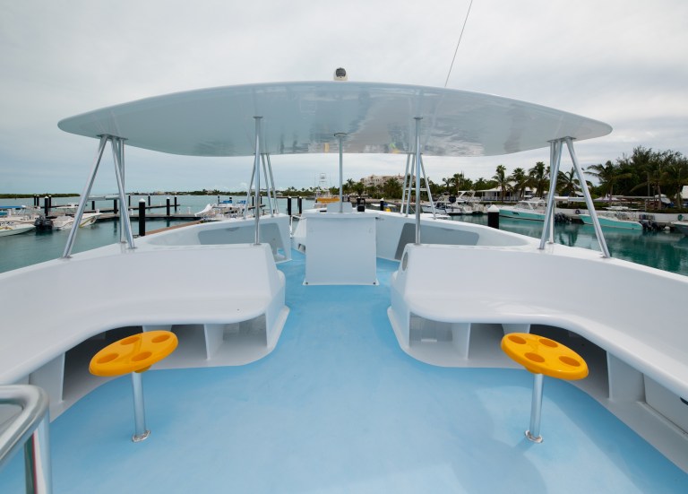 Boat deck with white seating and orange stools, docked at a marina.