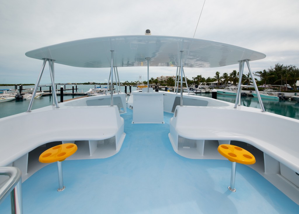 Boat deck with white seating and orange stools, docked at a marina.