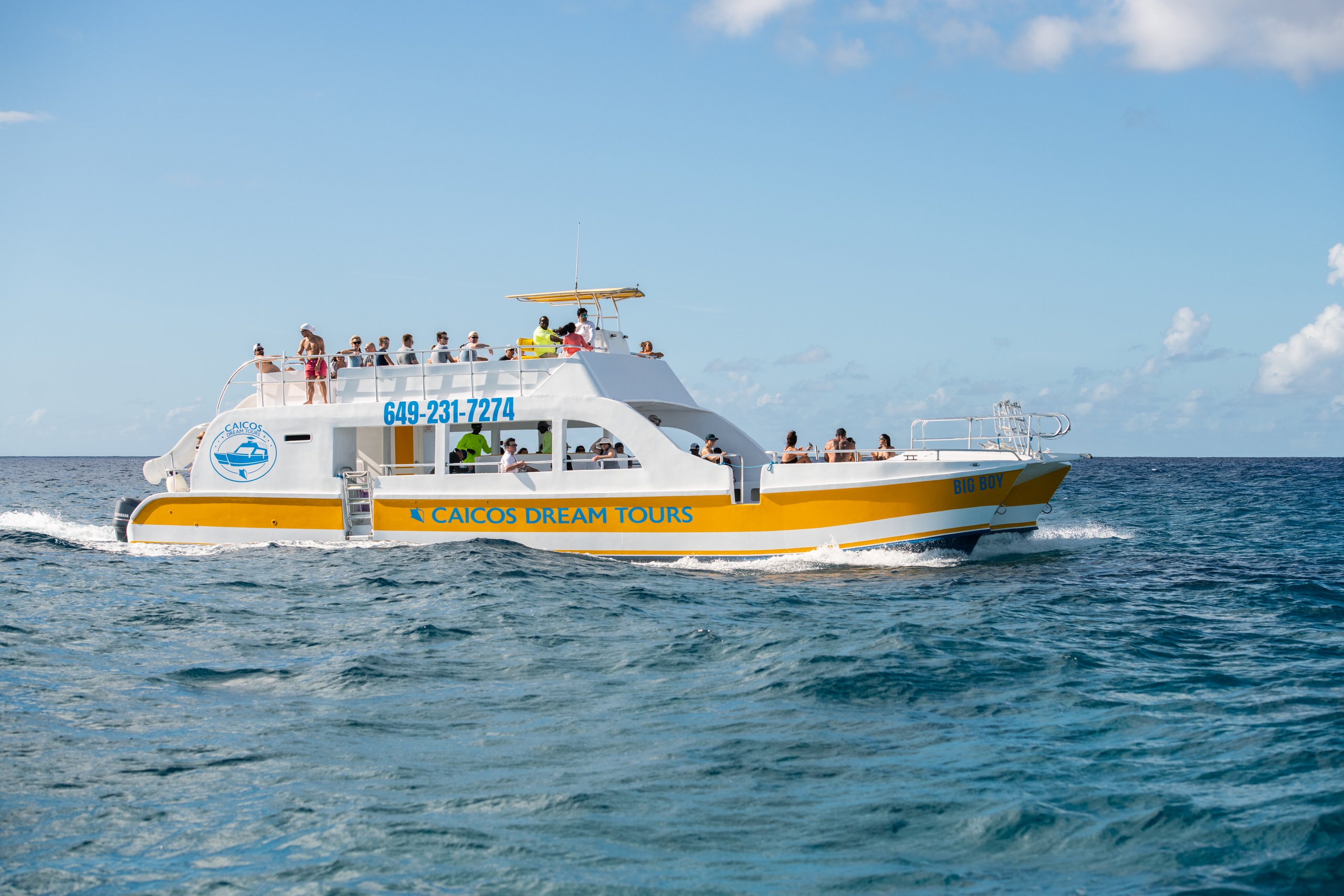 Yellow and white tour boat on ocean with passengers under clear sky.