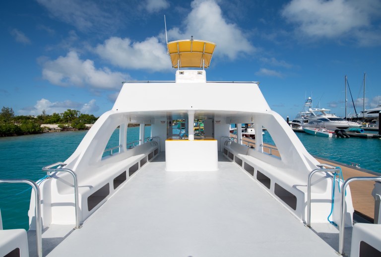 Empty ferry deck with canopy, docked by turquoise water under a blue sky.