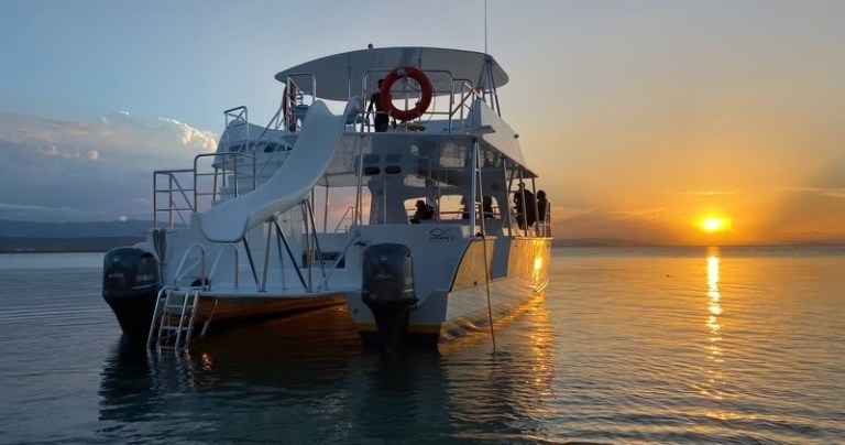 A boat with a slide on calm water at sunset.