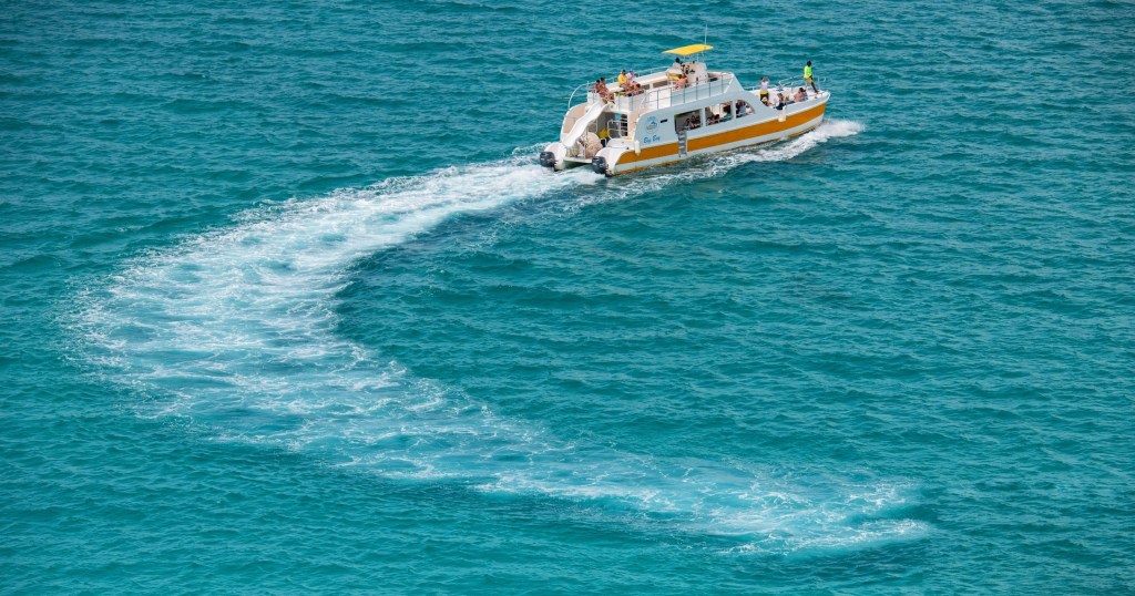 A boat making a curved trail on clear blue water.