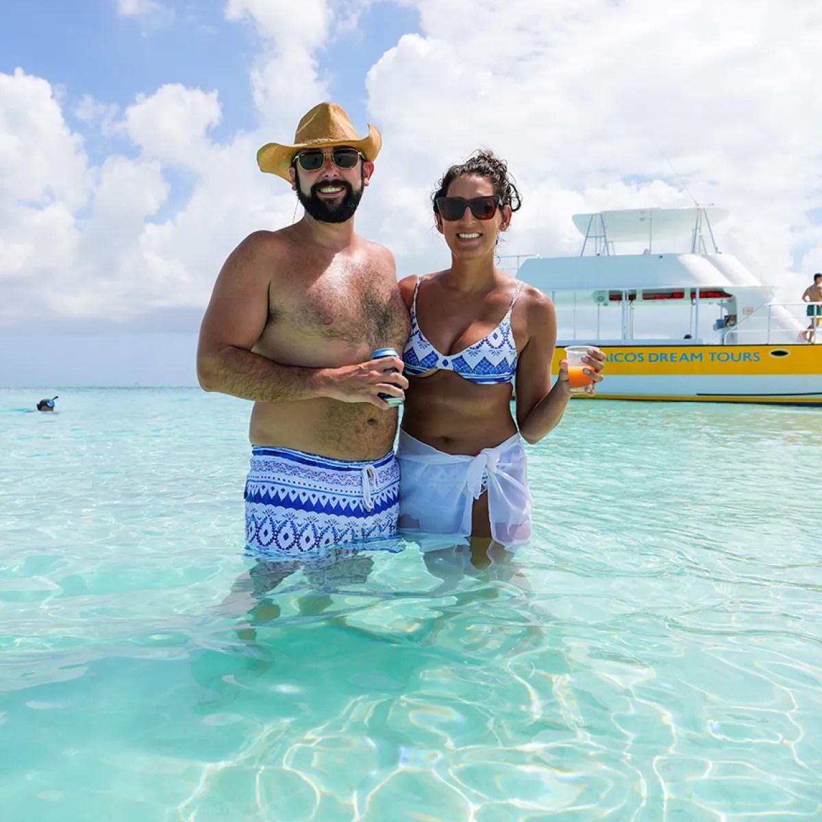 Couple in swimwear standing in clear blue water with a boat in the background.