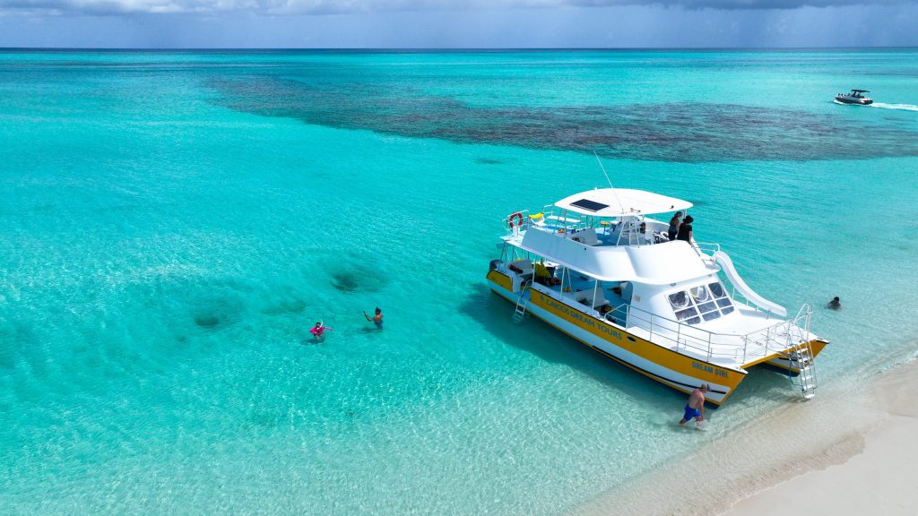 People swim near a large boat docked on clear turquoise water.