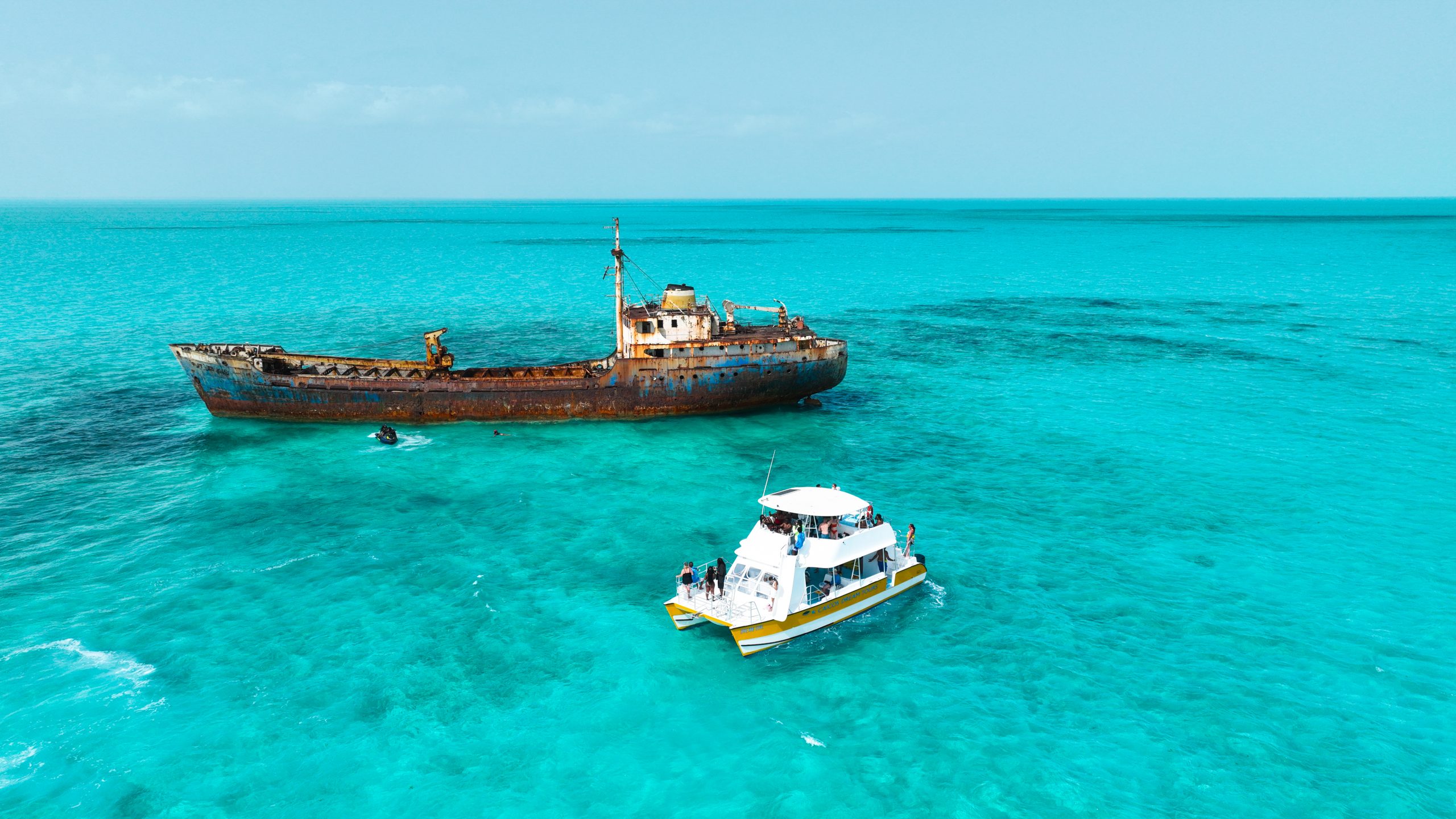 Small boat near a rusted shipwreck in clear turquoise water.