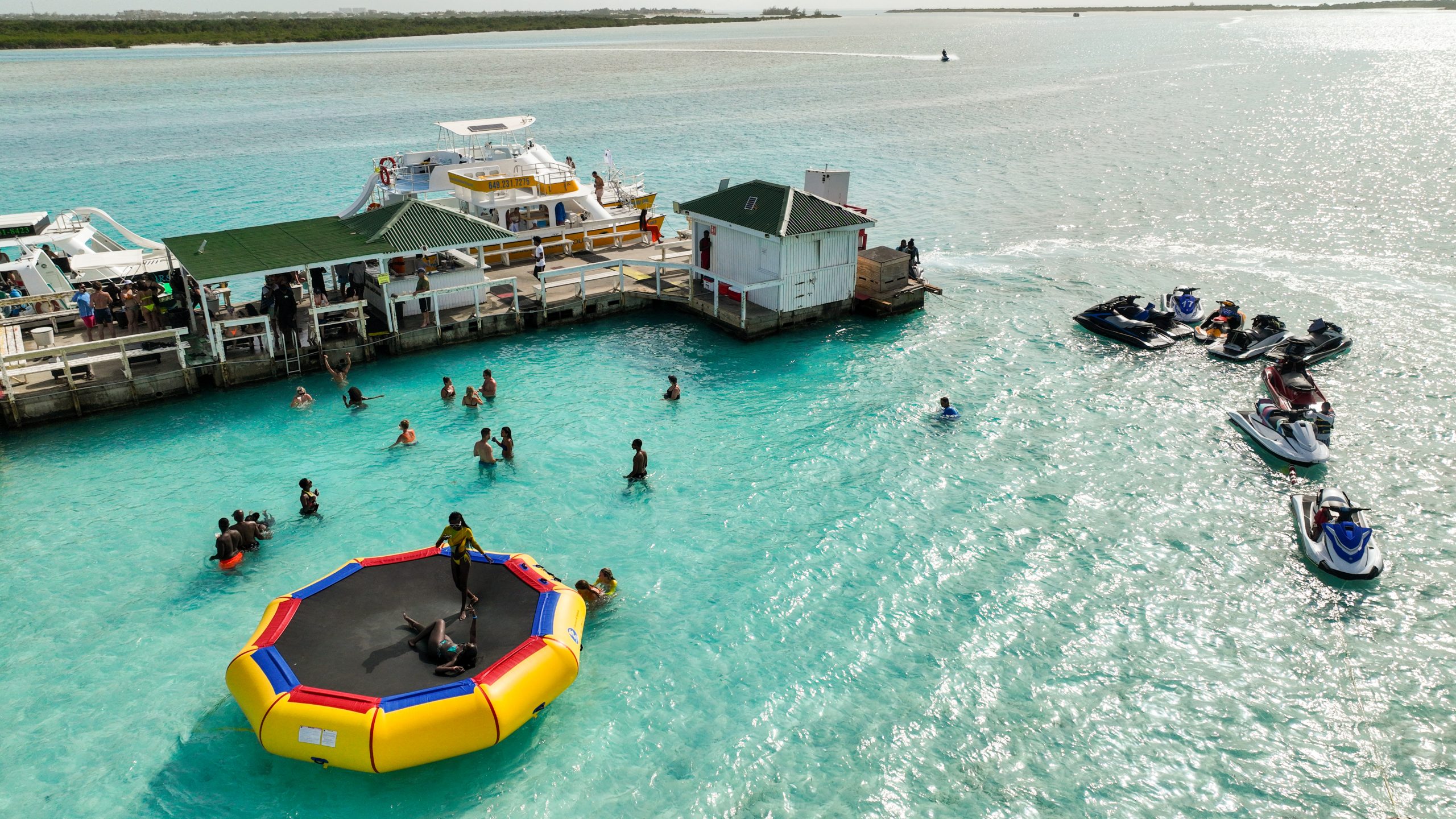 People enjoying water activities near a floating platform and jet skis.