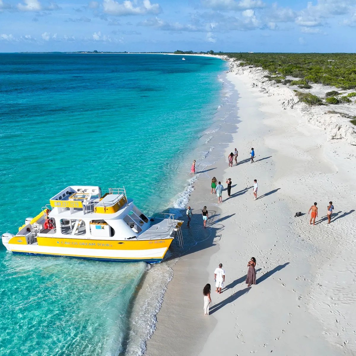 Yellow boat docked on sandy beach with people and turquoise water.