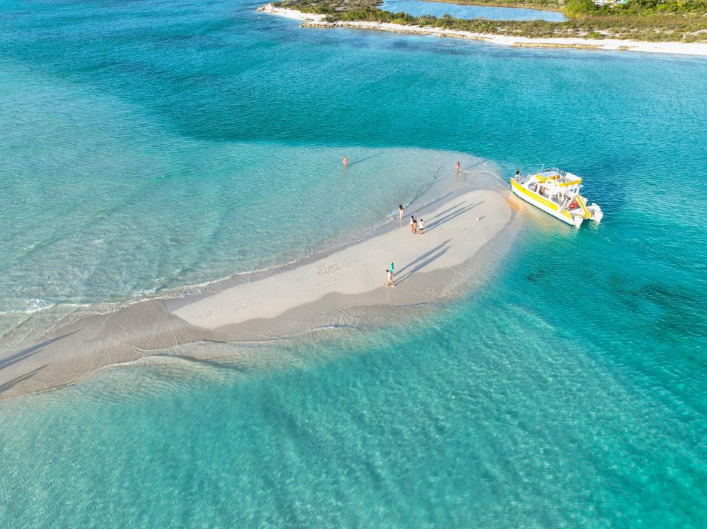 People on a small sandy island with a yellow boat in turquoise water.