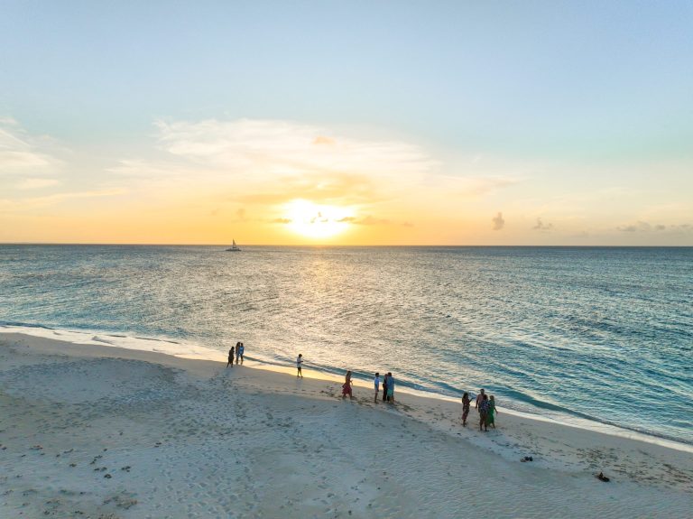 People on beach at sunset with sailboat in distance