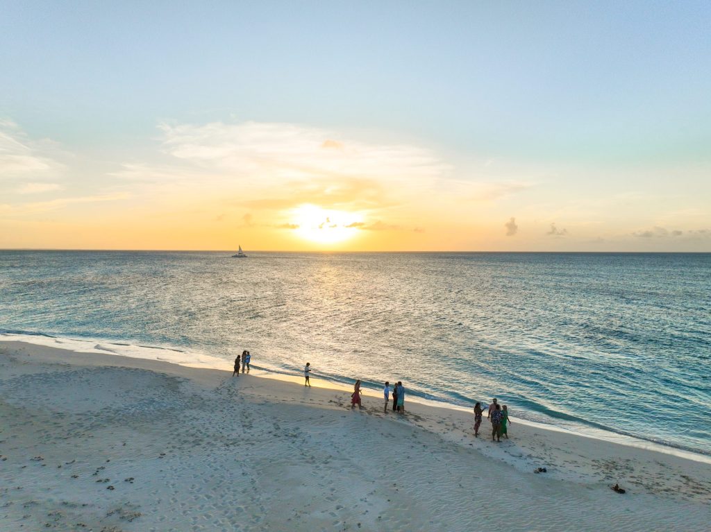People on beach at sunset with sailboat in distance