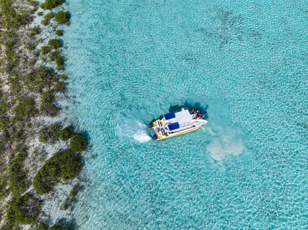 Aerial view of a boat in clear turquoise water near a small patch of lush greenery.
