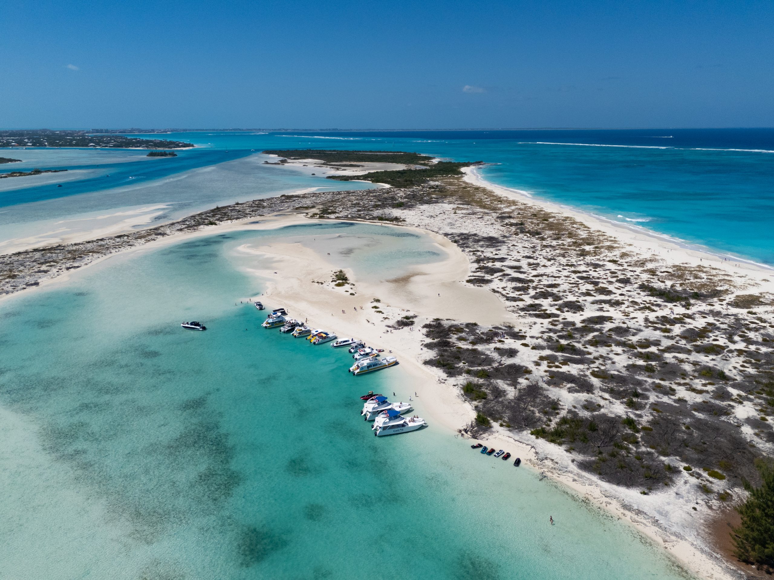 Aerial view of boats docked on a sandy beach with turquoise waters.