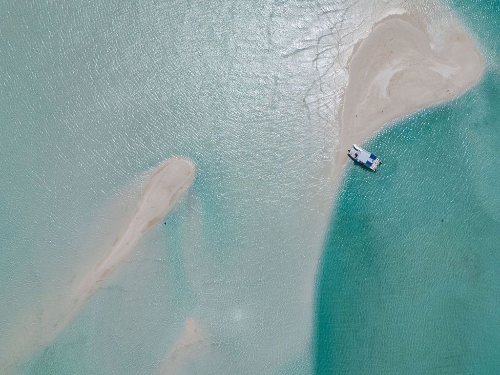 Aerial view of a boat near a sandy island in clear turquoise water.