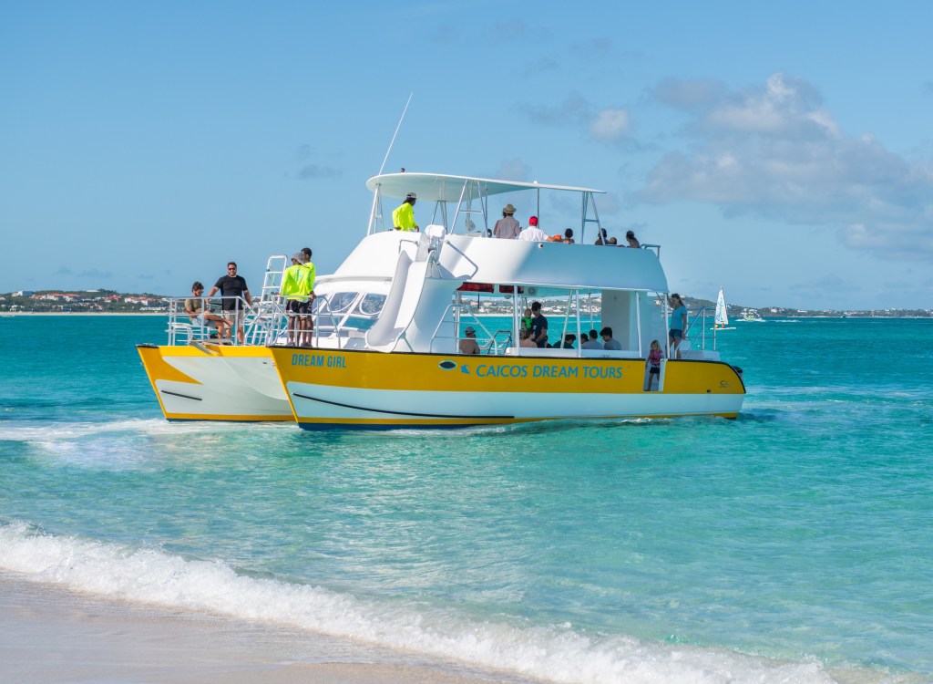 Two catamarans with tourists on turquoise ocean near a sandy beach.