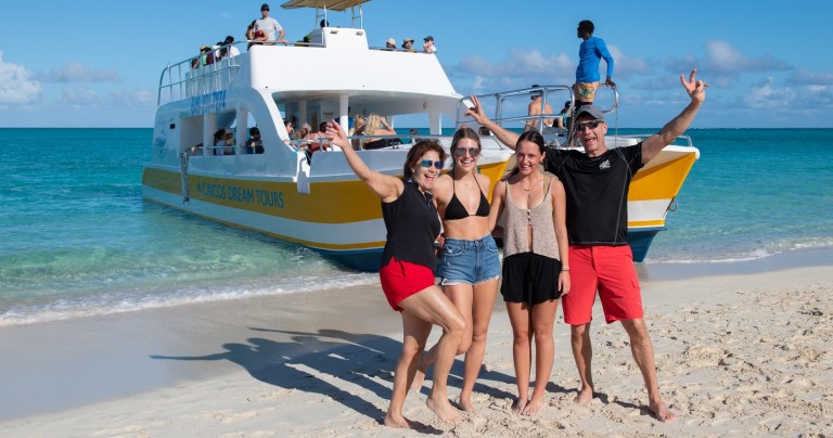Four people smiling on a beach with a boat in the background.
