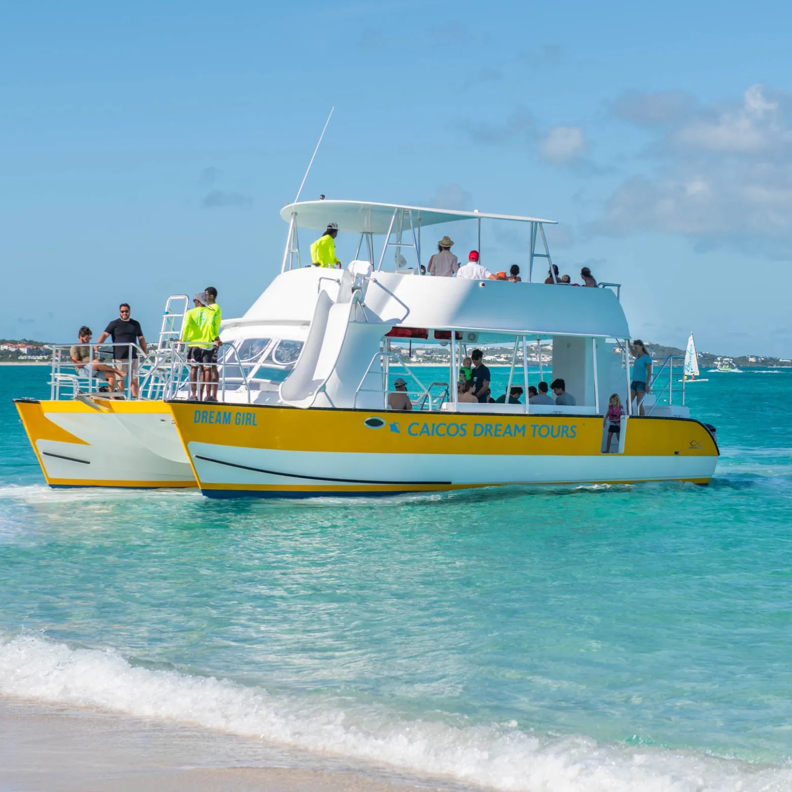 Yellow tour boat on turquoise water with people on deck.