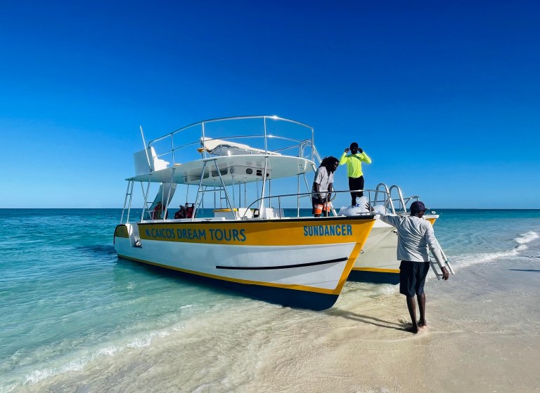 Tour boat on sandy beach with three people under clear blue sky.