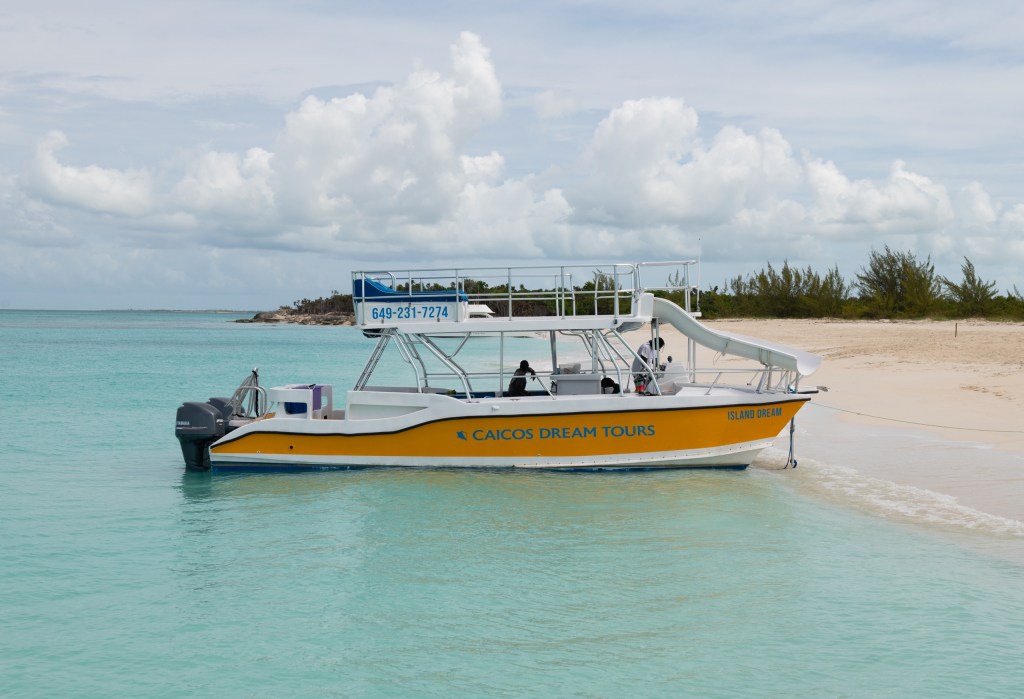 A yellow tour boat with a slide docked on a sandy beach.