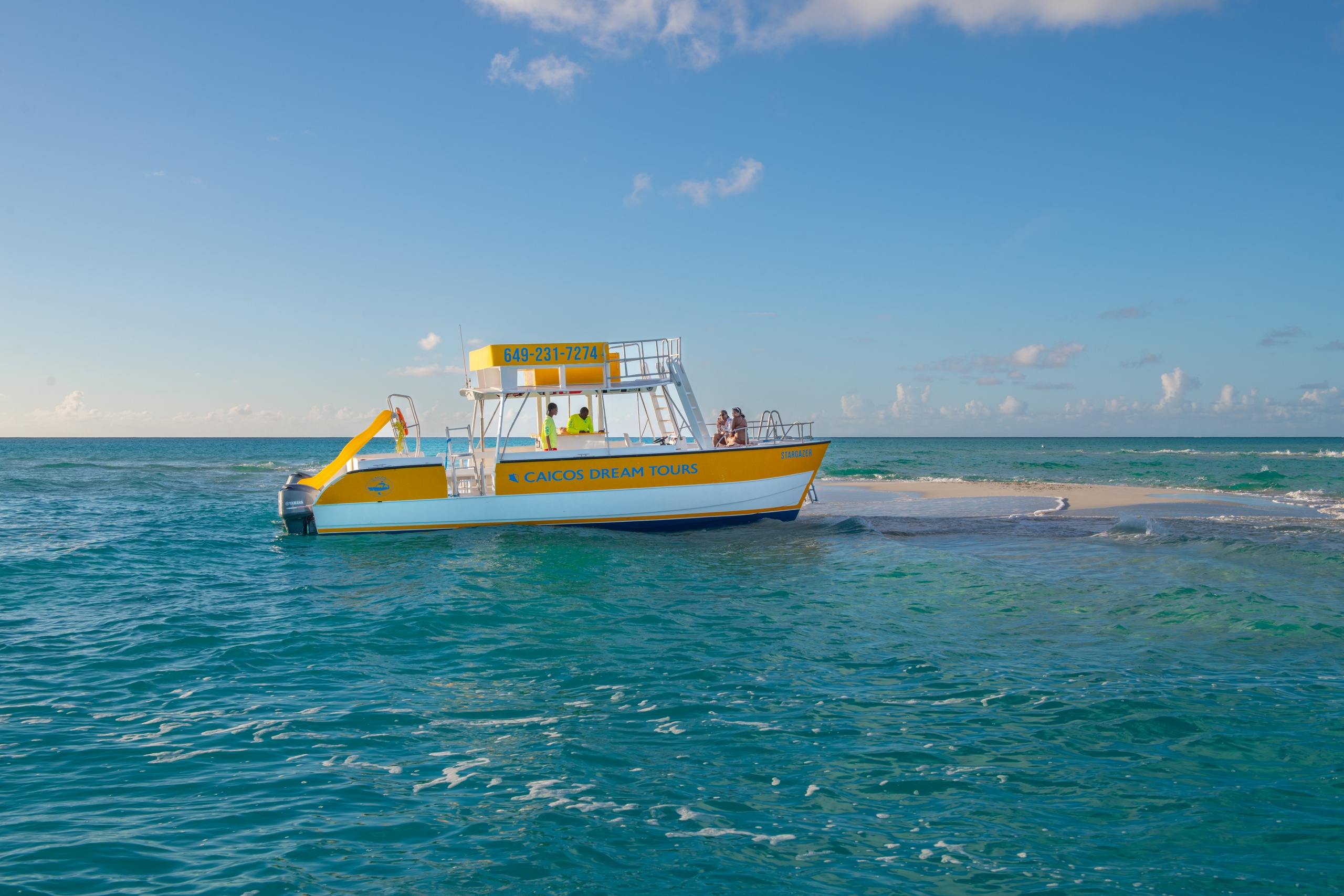 Yellow tour boat near a small sandy island in clear blue water.