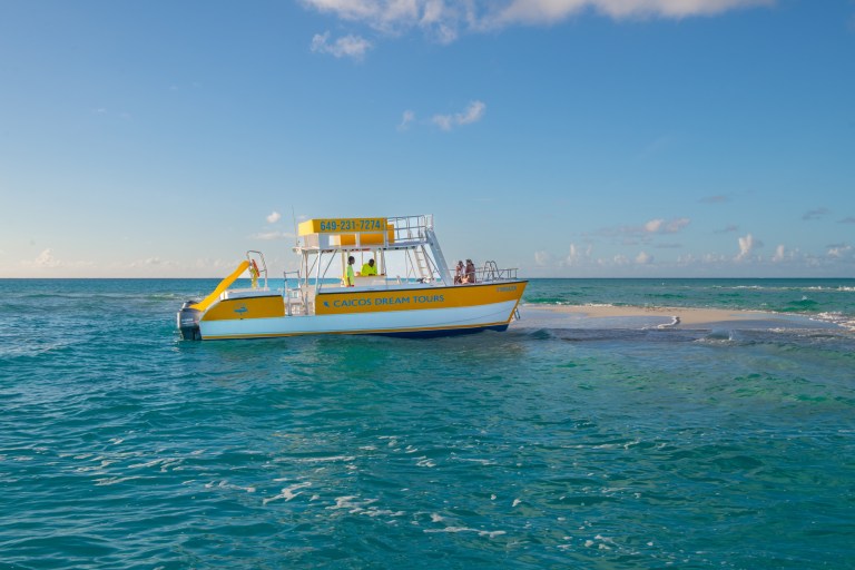 Yellow tour boat near a small sandy island in clear blue water.