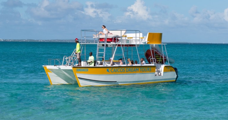 A tour boat with passengers floats on clear turquoise water under a partly cloudy sky.