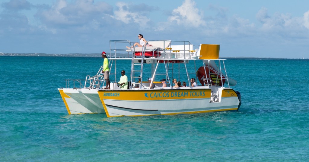 A tour boat with passengers floats on clear turquoise water under a partly cloudy sky.