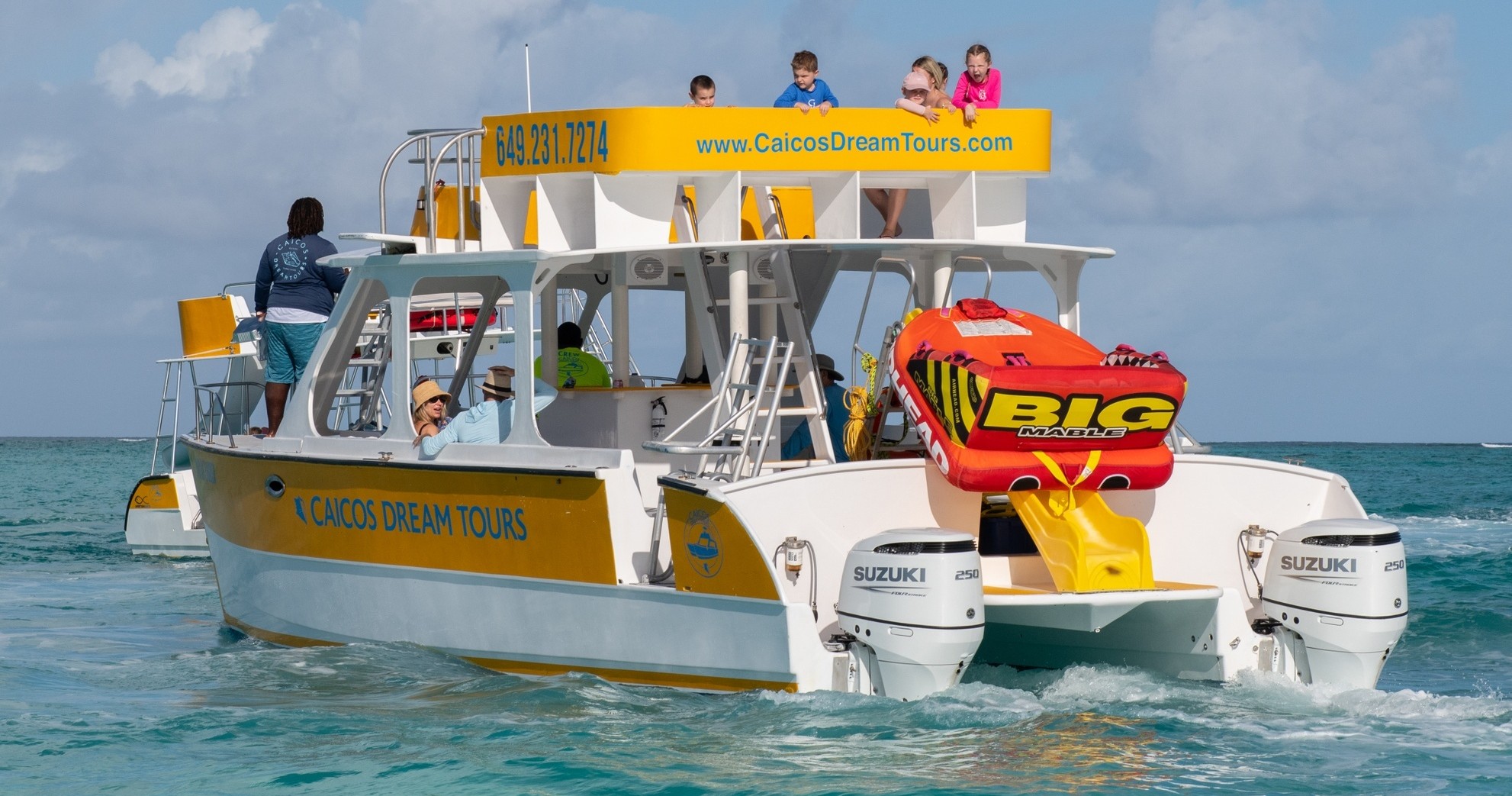 Catamaran boat with tourists and large inflatable in clear ocean water.