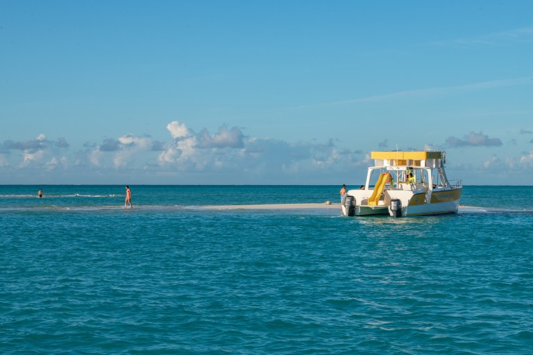 Boat docked on a small sandbar in blue ocean under a clear sky.