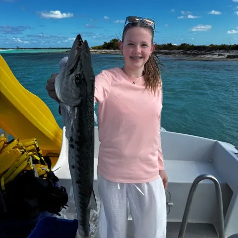 Person on a boat holding a large fish, with water and coastline in the background.