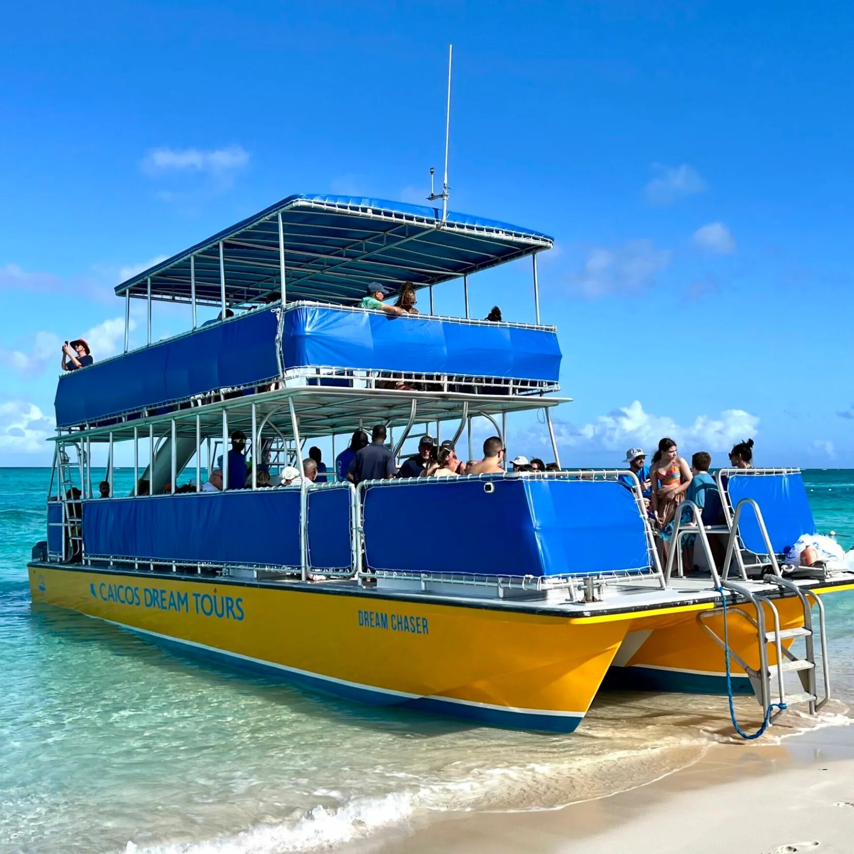 Blue and yellow boat on a beach, people onboard, clear sky.