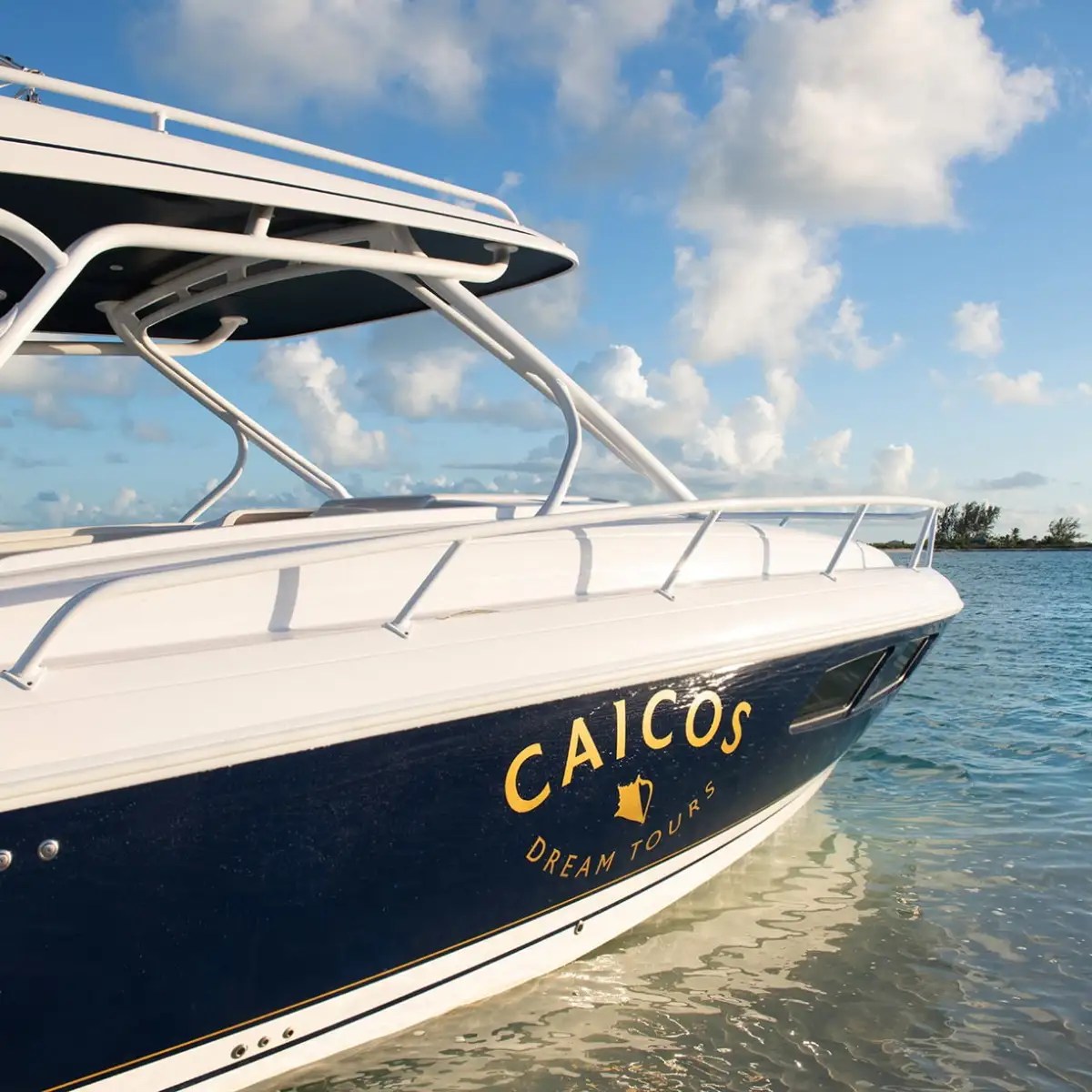 White and blue boat named Caicos on clear water under a blue sky.