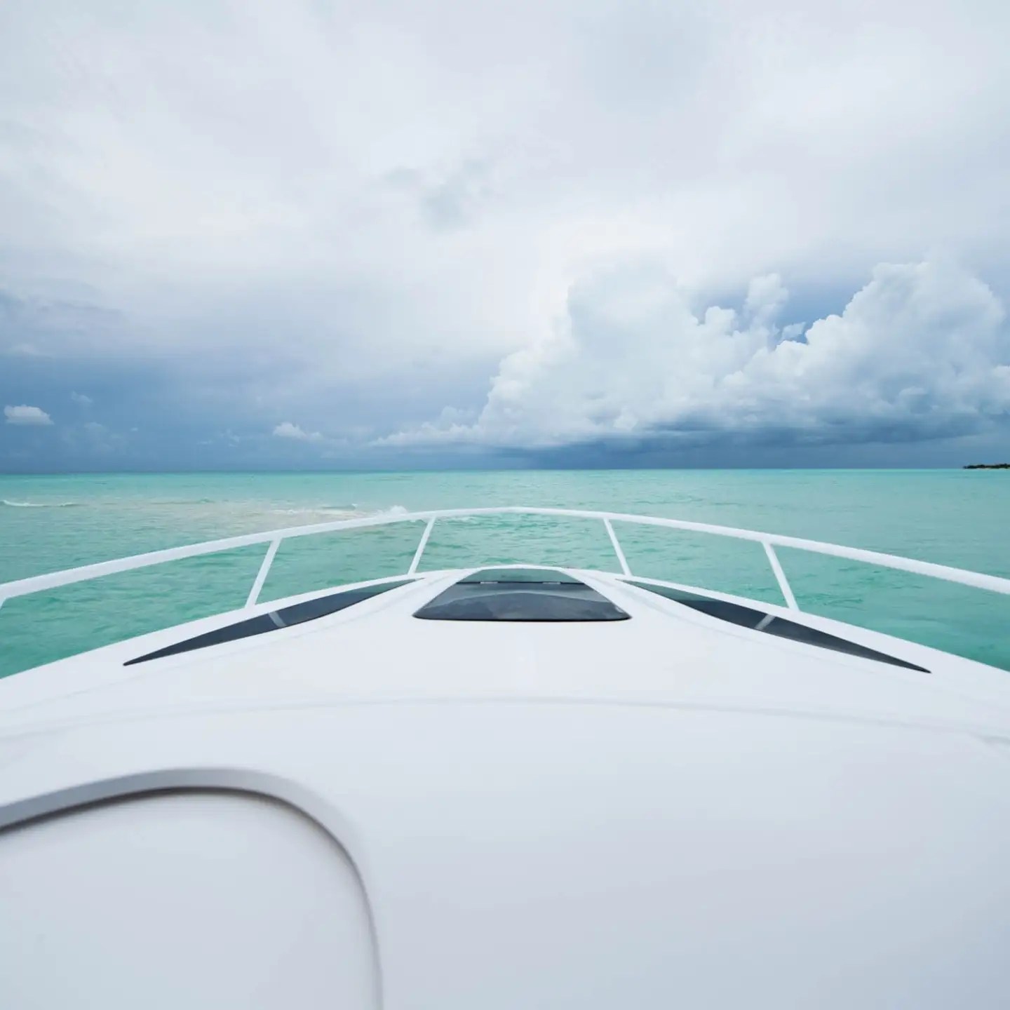View from a boat's bow facing calm turquoise sea and cloudy sky.