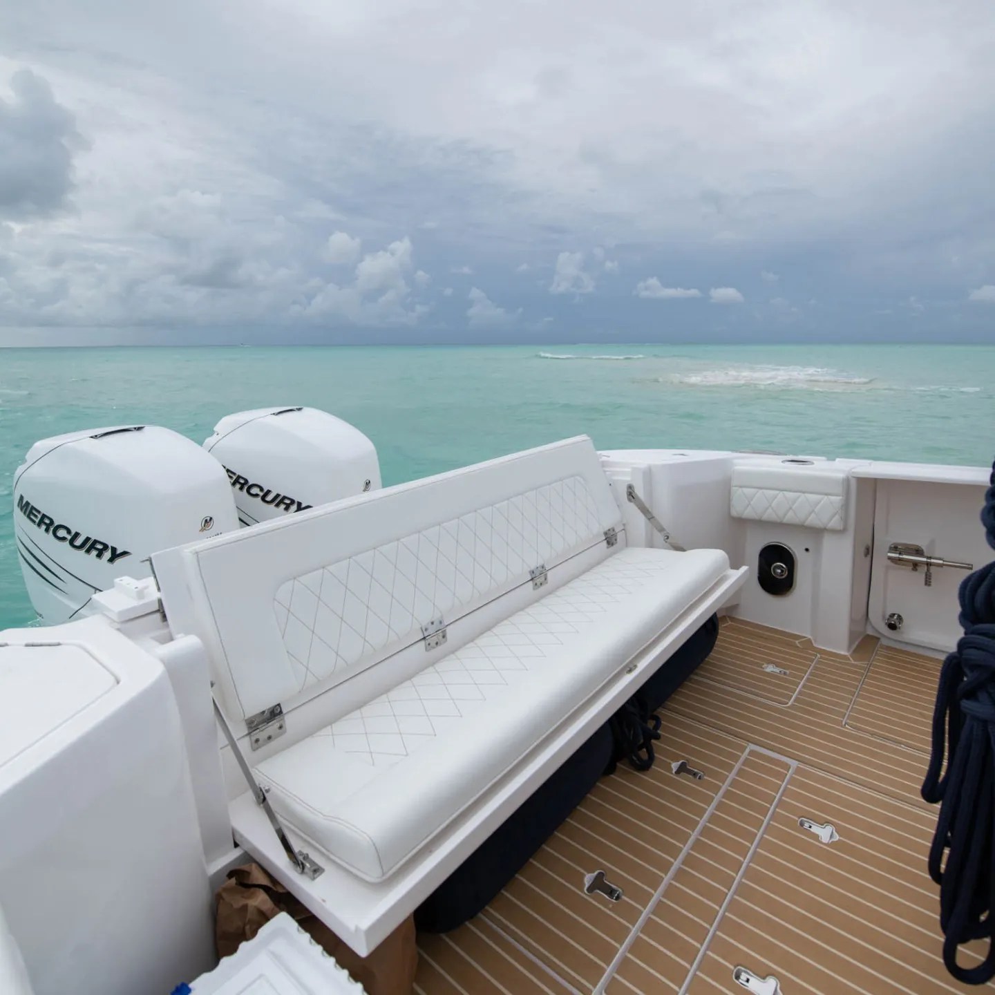 Boat deck with white seats and ocean view under cloudy sky.
