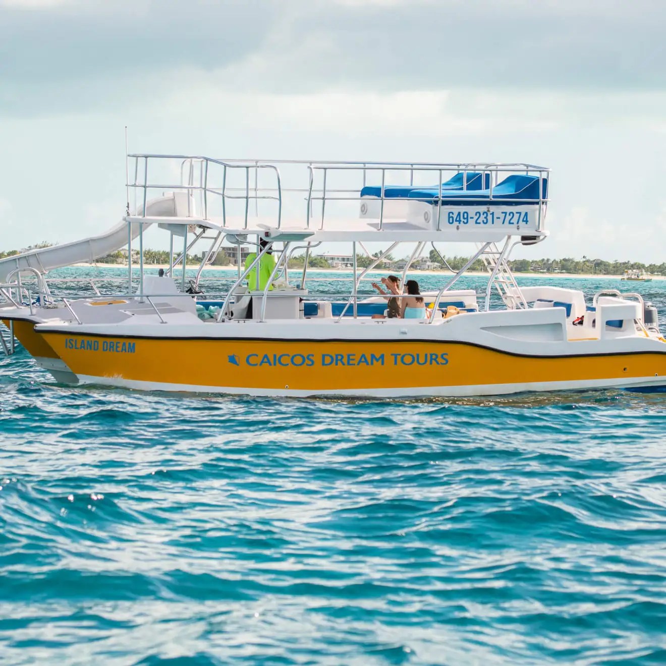 A yellow tour boat named 'Caicos Dream' on a calm sea under a cloudy sky.