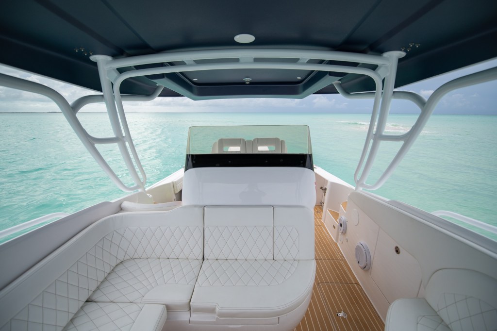 Interior of a luxury boat with white seating and wooden floor, overlooking turquoise water.